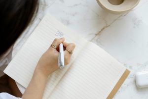 A woman writes in a notebook at a marble table, creating a peaceful scene of creativity.